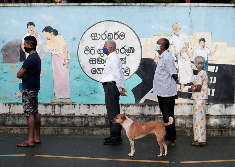 People wearing protective masks wait in a line outside a polling station as they prepare to cast their vote in Colombo