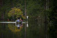 In this Friday, Sept. 21, 2018 photo, Kristen and Jason Atoigue Burgaw pilot a boat through floodwaters after visiting their house to retrieve their flood insurance papers and their son's hamster in Pender County, N.C. The Atoigues sustained a few feet of water in their residence. (Kristen Zeis/The Virginian-Pilot via AP)