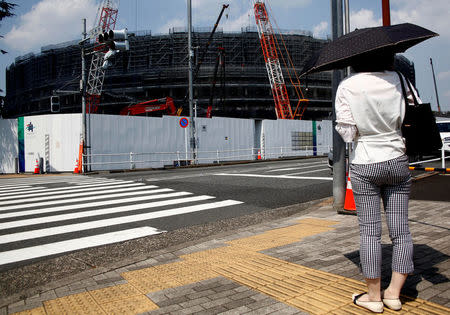 A woman holding a parasol stands in front of the construction site of the New National Stadium, the main stadium of the Tokyo 2020 Olympics and Paralympic in Tokyo, Japan July 24, 2018. REUTERS/Kim Kyung-Hoon