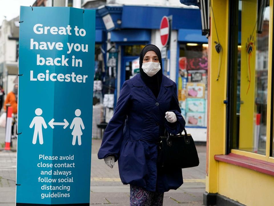 A woman wearing a PPE mask walks past social distance advisory signs in Leicester's North Evington neighbourhood on June 29, 2020 in Leicester, England: Getty