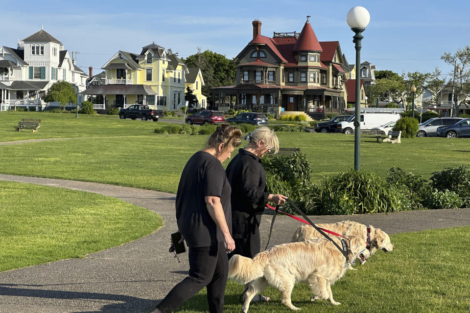 People walk dogs in front of homes, Tuesday, June 4, 2024, in Oak Bluffs, Massachusetts. High housing costs on Martha's Vineyard are forcing many regular workers to leave and are threatening public safety. (AP Photo/Nick Perry)