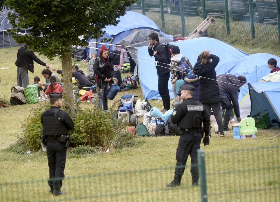 French police officers watch migrants packing their belongings in a camp of Grande Synthe, northern France, Tuesday, Sept.17, 2019. French police are evacuating at least 900 migrants from a gym near the English Channel, citing concerns about security and hygiene. (AP Photo)