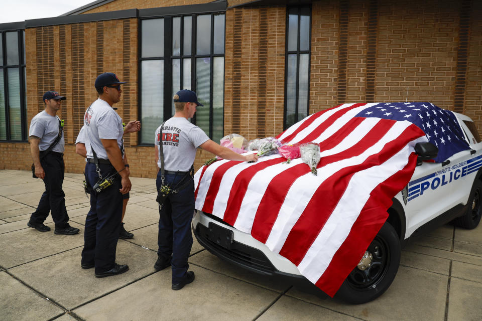 Charlotte firefighters from Engine 7 bring flowers to a flag-covered Charlotte-Mecklenburg police vehicle at the North Tryon Station in Charlotte, N.C., Tuesday, April 30, 2024, where Charlotte-Mecklenburg Officer Joshua Eyer was stationed. Police in North Carolina say a shootout that killed several law enforcement officers, including Eyer, and wounded others began as officers approached a home on Monday to serve a warrant for a felon wanted for possessing a firearm. (AP Photo/Nell Redmond)