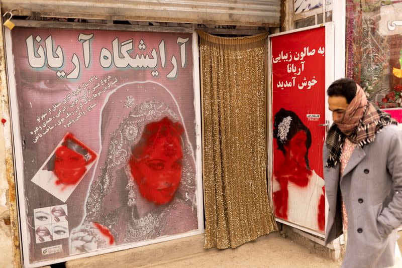 A man walks past a beauty shop with defaced pictures of women in Kabul