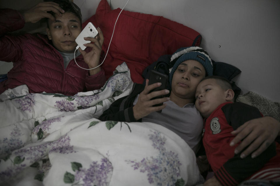 ARCHIVO - En esta foto del 8 de febrero del 2019, el migrante hondureño Josué Mejía Lucero, de 17 años, su novia Milagro de Jesús Henríquez Ayala, de 15, y Jefferson, de 3 años y sobrino de Josué, miran a celulares en su cama en el Albergue de la Misión Mundial Agape en Tih¡juana, México. Atrás han quedado las costosas llamadas telefónicas con familiares y amigos en Estados Unidos para decidir la ruta o la búsqueda del mejor “coyote”, del traficante. Ahora crean un grupo de chat y se organizan para salir en caravana. (AP Foto/Emilio Espejel)