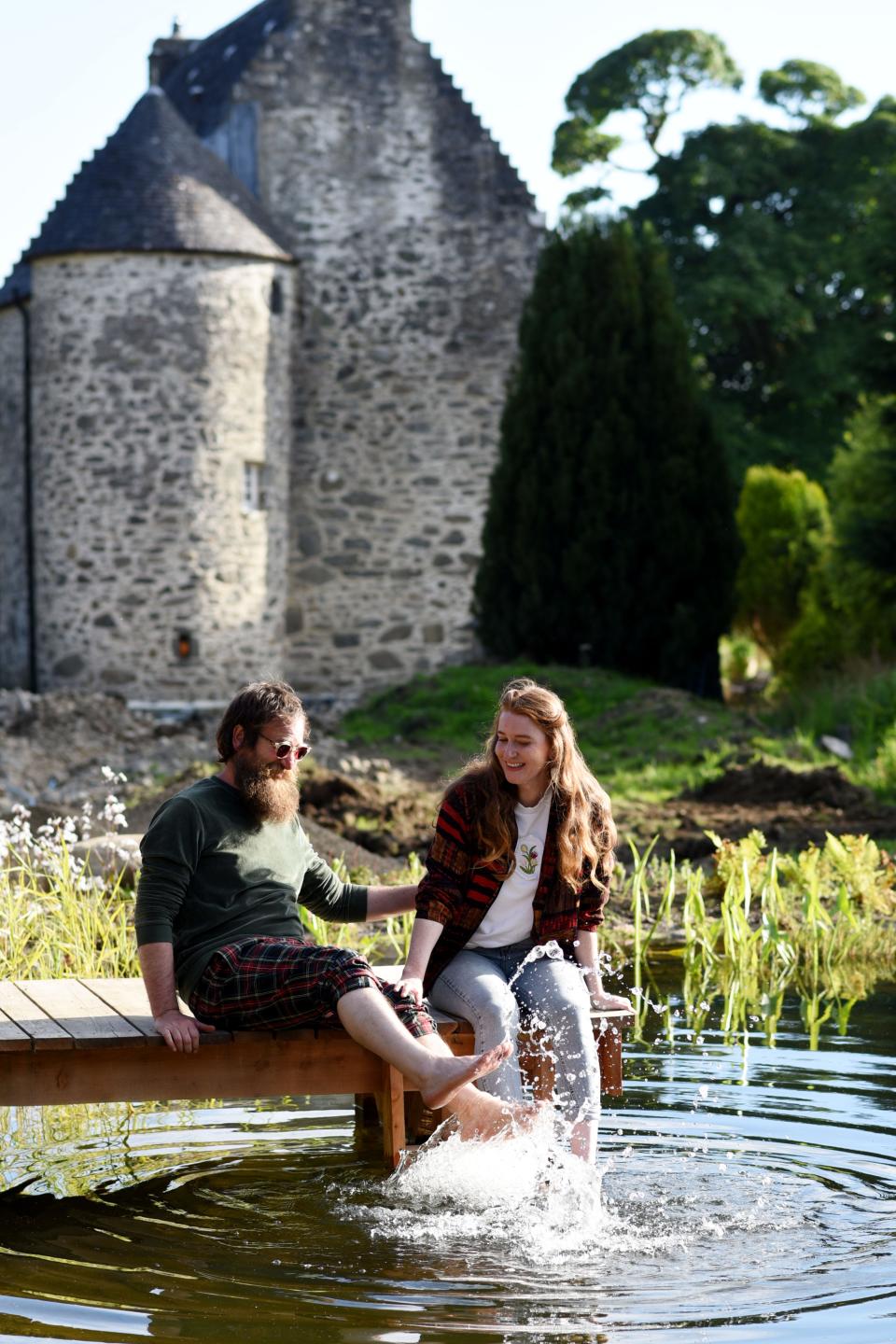 Stef Burgon and Simon Hunt, owners of Kilmartin Castle, are pictured sitting on the dock next to their wild swimming pond.