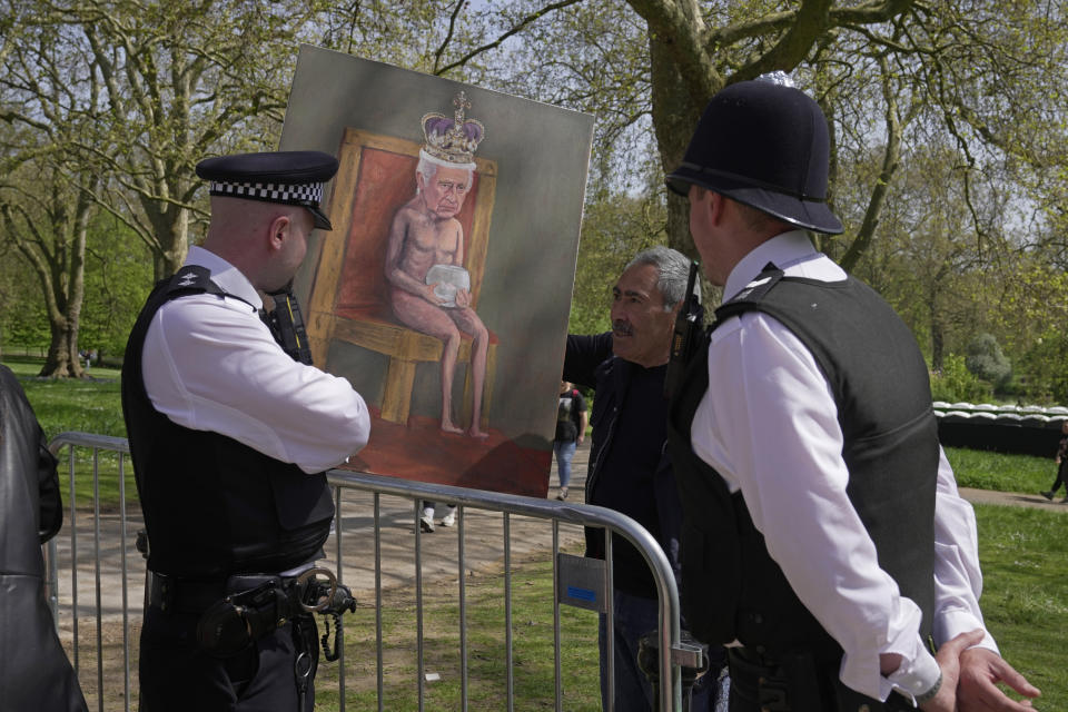 Artist Kaya Mar, center, shows his painting depicting King Charles III to police officers along the King's Coronation route at The Mall in London, Wednesday, May 3, 2023. The Coronation of King Charles III will take place at Westminster Abbey on May 6. (AP Photo/Kin Cheung)