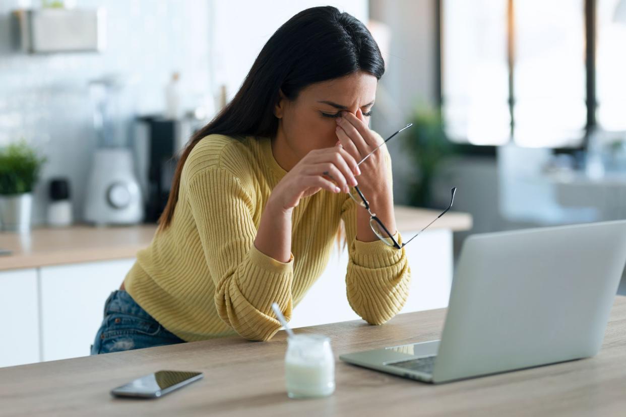 Shot of stressed business woman working from home on laptop looking worried, tired and overwhelmed while sitting in the kitchen at home.