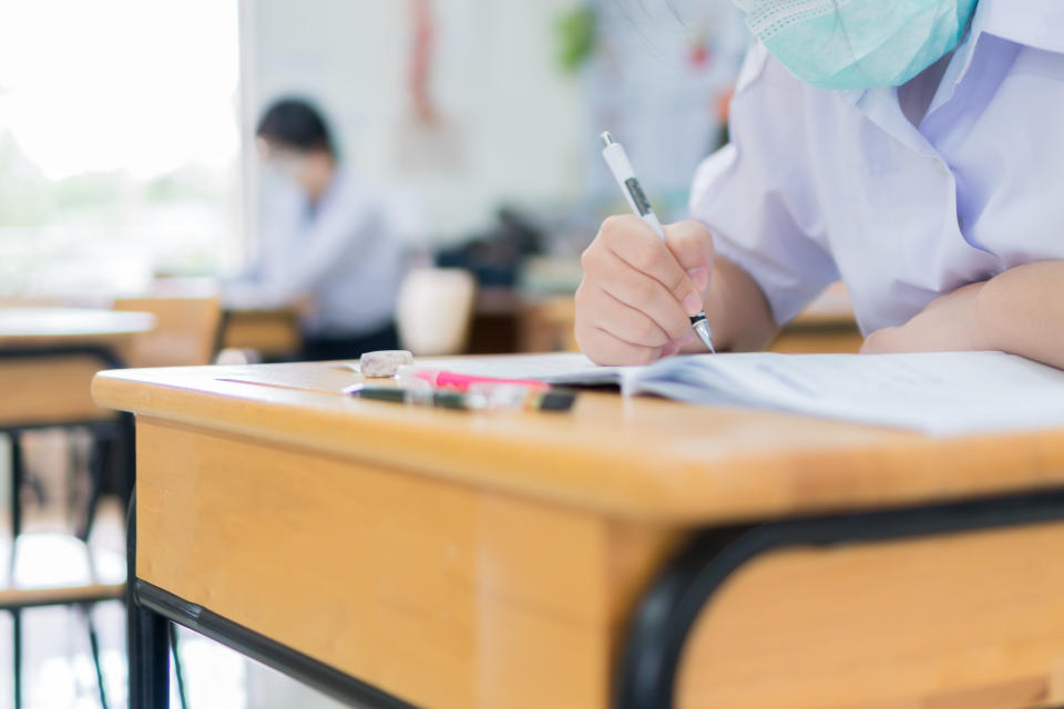 Asian Student girls wear face mask prevent COVID-19 coronavirus in Classroom for final test education exam room on High school. Students hold pencil writing paper documents for taking exams in room