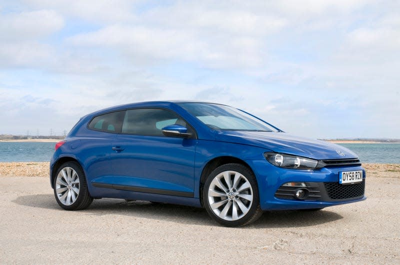 An image of a navy blue third-generation VW Scirocco parked in a beachside parking lot.