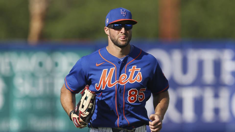 Tim Tebow jogs while wearing a blue Mets jersey and cap.