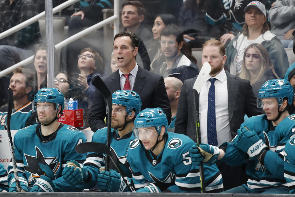 FILE - San Jose Sharks head coach David Quinn and assistant coach Ryan Warsofsky, obscured by a hockey stick, are shown behind the bench in the third period of an NHL hockey game against the Columbus Blue Jackets in San Jose, Calif., Tuesday, March 14, 2023. The San Jose Sharks have promoted Ryan Warsofsky to become the team's new head coach after two years as an assistant under the recently fired David Quinn. General manager Mike Grier announced Thursday, June 13, 2024, that Warsofsky will become the 11th head coach in franchise history. (AP Photo/Josie Lepe, File)