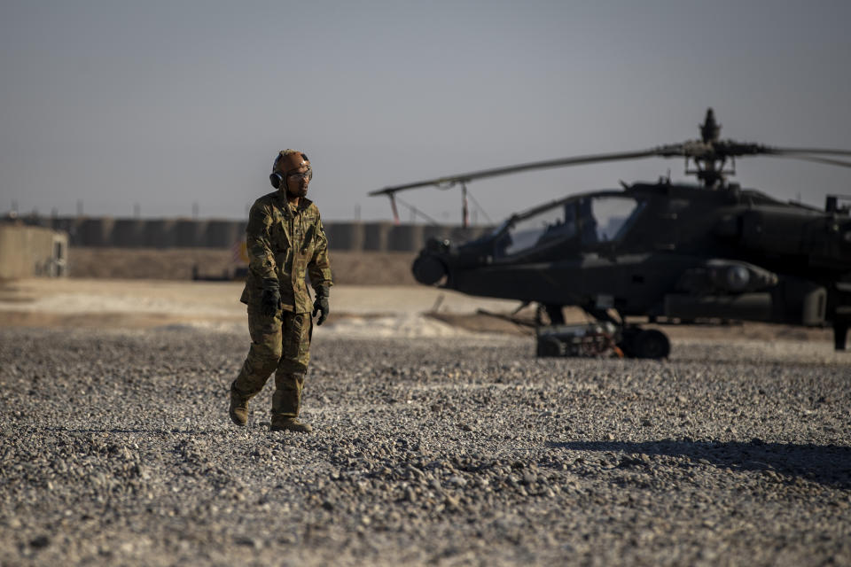 A crewman walks past an attack helicopter at a US military base at an undisclosed location in eastern Syria, Monday, Nov. 11, 2019. The deployment of the mechanized force comes after US troops withdrew from northeastern Syria, making way for a Turkish offensive that began last month. (AP Photo/Darko Bandic)