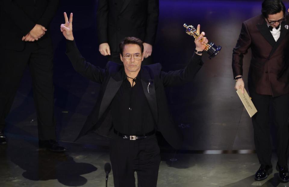 Robert Downey Jr. makes a peace sign with his hand and holds up an Oscar.