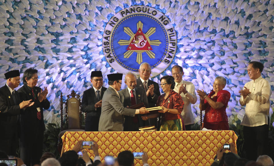 In this handout photo released by the Malacanang Photo Bureau, President Benigno S. Aquino III, third from right, Moro Islamic Liberation Front (MILF) Chairman, Al Haj Murad Ebrahim, third from left, Malaysian Prime Minister Najib Razak, center, and Secretary Teresita Quintos-Deles, Presidential Adviser on the Peace Process, second from right, applaud as they witness the exchange of the signed Comprehensive Agreement on the Bangsamoro (CAB) by MILF chief negotiator Mohagher Iqbal, fourth from left, and Miriam Coronel Ferrer, fourth from right, of the Philippine government in a ceremony at the Malacanang Presidential Palace in Manila, Philippines on Thursday March 27, 2014. The Philippine government signed a peace accord with the country's largest Muslim rebel group on Thursday, the culmination of years of negotiations and a significant political achievement for President Aquino.(AP Photo/Malacanang Photo Bureau, Ryan Lim)