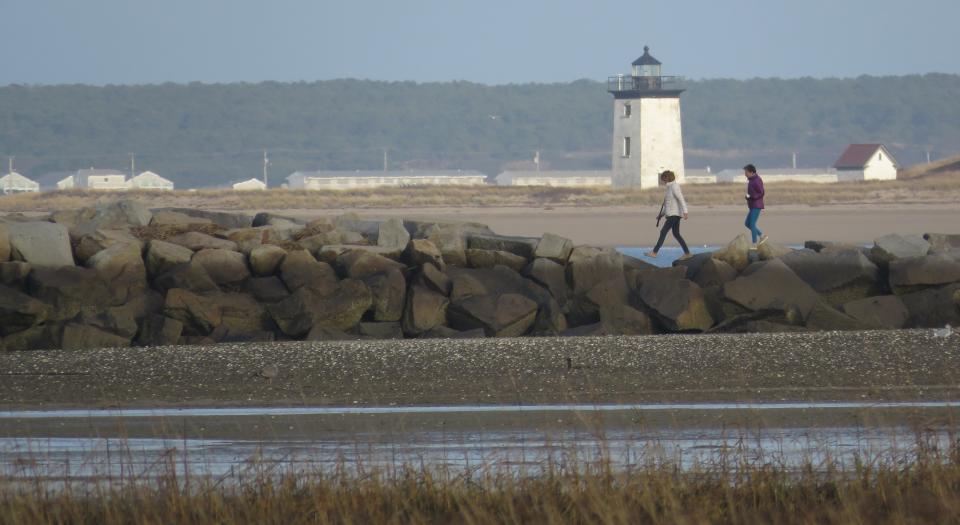 Brave hikers conquer the Provincetown breakwater, with Long Point Light in the background.