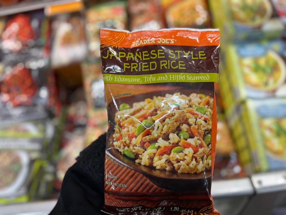 A hand holds a brown and orange bag with a green label and a picture of fried rice with edamame, tofu, and carrots