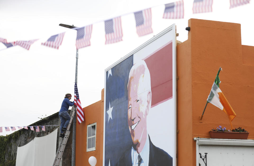 A man puts a US flag up near the mural of President elect Joe Biden, in the town of Ballina, North West of Ireland, Saturday, Nov. 7, 2020. Biden was elected Saturday as the 46th president of the United States, defeating President Donald Trump in an election that played out against the backdrop of a pandemic, its economic fallout and a national reckoning on racism. (AP Photo/Peter Morrison)