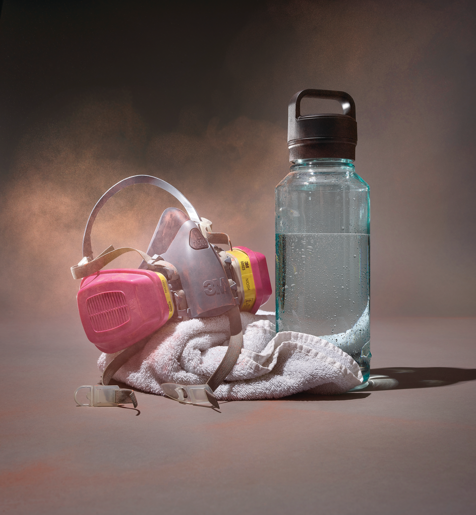 still life of a water bottle sweat towel and industrial face mask with orange air swirling around