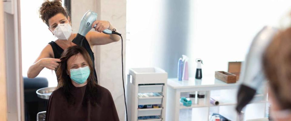 Working during covid-19 or coronavirus concept. A professional hairdresser cutting the hair to a client, reflected in the mirror with copy space.