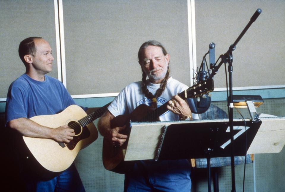 Willie Nelson and another playing guitar in a music studio, with microphones and music stands visible