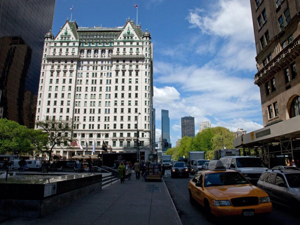 A photo of the Plaza Hotel, which has several condos as well as hotel rooms, in Midtown Manhattan. A yellow cab and Central Park can be seen to the right of the photo.