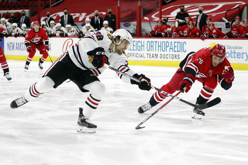 Chicago Blackhawks' Alex DeBrincat (12) shoots the puck past Carolina Hurricanes' Brady Skjei (76) during the first period of an NHL hockey game in Raleigh, N.C., Thursday, May 6, 2021. (AP Photo/Karl B DeBlaker)