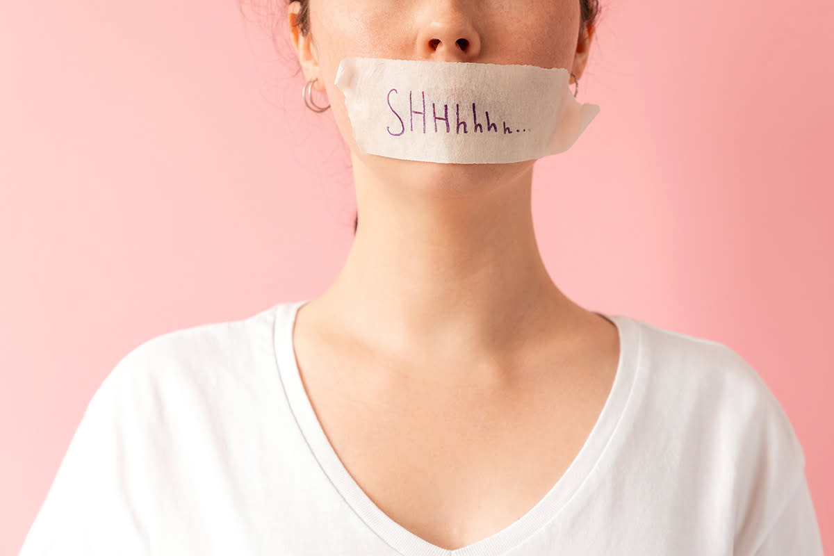 Close up of caucasian woman's face with her mouth taped shut. Tape has the inscription Shhh. Pink background. The concept of women's secrets and problems.