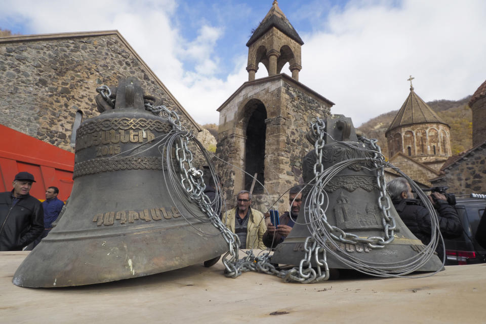 People look at bells, removed form the Dadivank, an Armenian Apostolic Church monastery dating to the 9th century, as ethnic Armenians leave the separatist region of Nagorno-Karabakh to Armenia, Saturday, Nov. 14, 2020. The territory is to be turned over to Azerbaijan on Sunday as part of territorial concessions in an agreement to end six weeks of intense fighting with Armenian forces. Hundreds of thousands of Azeris were displaced by the war that ended in 1994. It is unclear when any civilians might try to settle in Karvachar — which will now be known by its Azeri name Kalbajar — or elsewhere. (AP Photo/Dmitry Lovetsky)