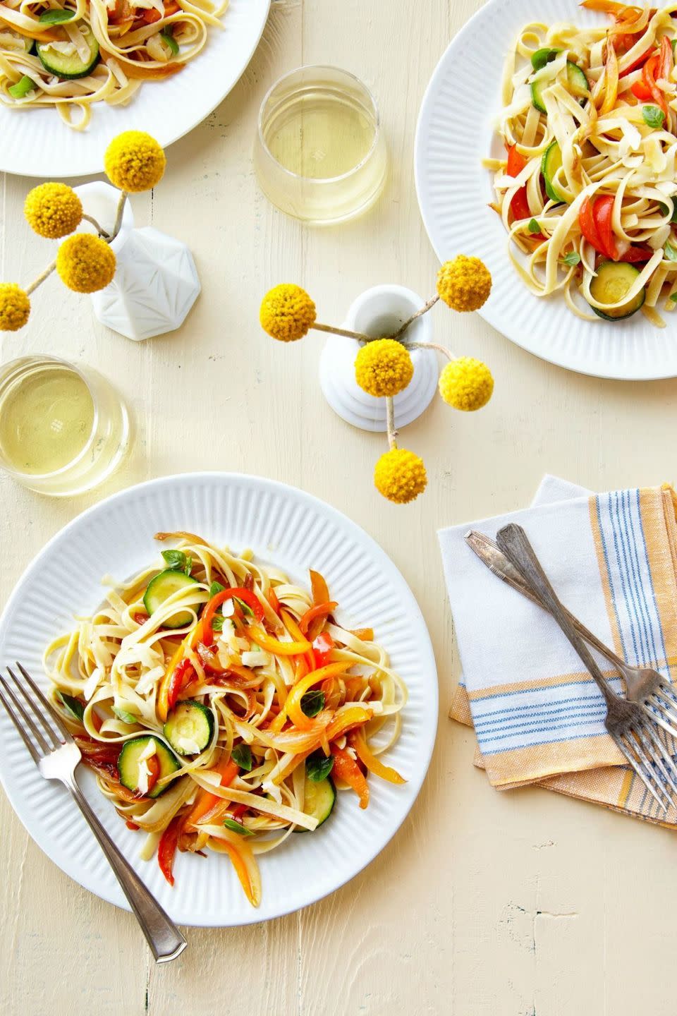 pasta with sauteed peppers, zucchini, and smoked mozzarella on a plate shot from overhead with these funny little yellow ball flowers in a vase on the same table