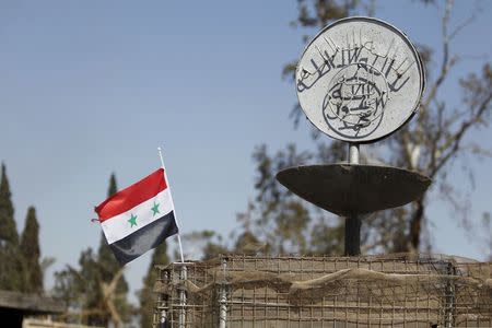 A Syrian national flag flutters next to the Islamic State's slogan at a roundabout where executions were carried out by ISIS militants in the city of Palmyra, in Homs Governorate, Syria in this April 1, 2016 file photo. REUTERS/Omar Sanadiki/Files