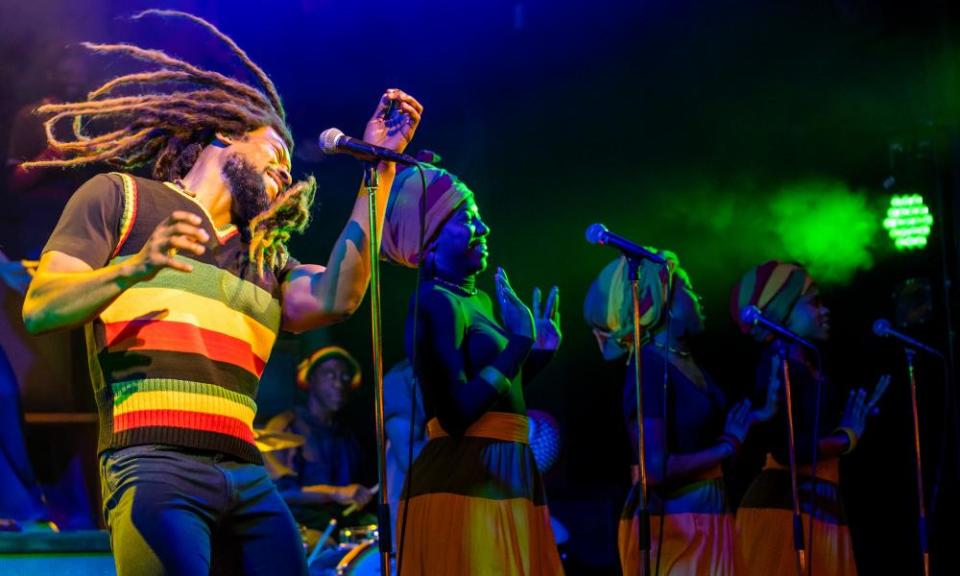 Actor with long dreadlocks dancing in front of a microphone, with female singers in the background