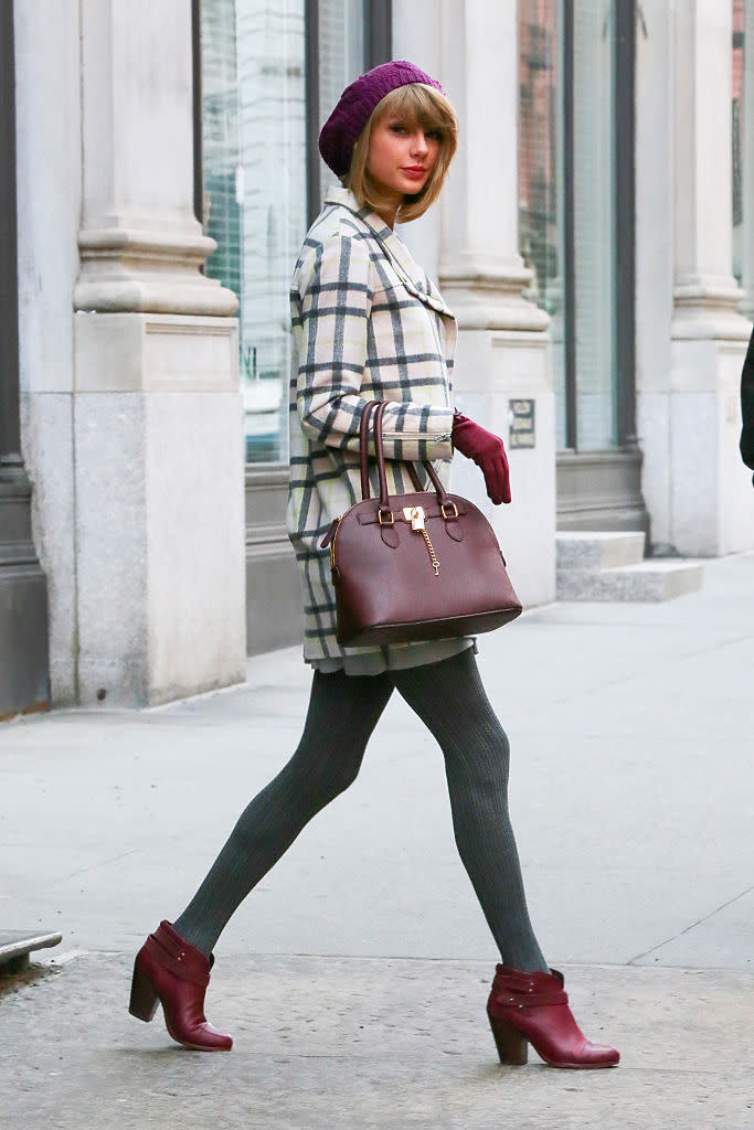 Petit look de rue très travaillé. La star est chic avec son manteau en tartan et ses collants en laine gris. Taylor Swift n’oublie jamais les détails et fait un rappel de couleur entre ses gants, son sac et ses chaussures.  