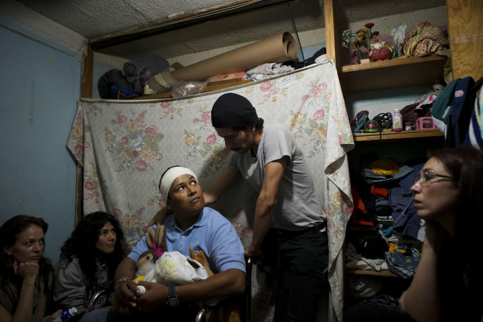 In this April 11, 2014 photo, Martin Camarillo, 35, who was paralyzed by a bullet when he was 19, performs a scene with actor Raul Briones as spectators crowd around them in Camarillo's cramped bedroom in Mexico City's Tepito neighborhood. Camarillo said he wants to show the visitors how similar their lives are. "We want for people to know that in Tepito there are also people who work hard, who set up their stands early in the morning to give their family a better future, to give them hope," he said. (AP Photo/Rebecca Blackwell)