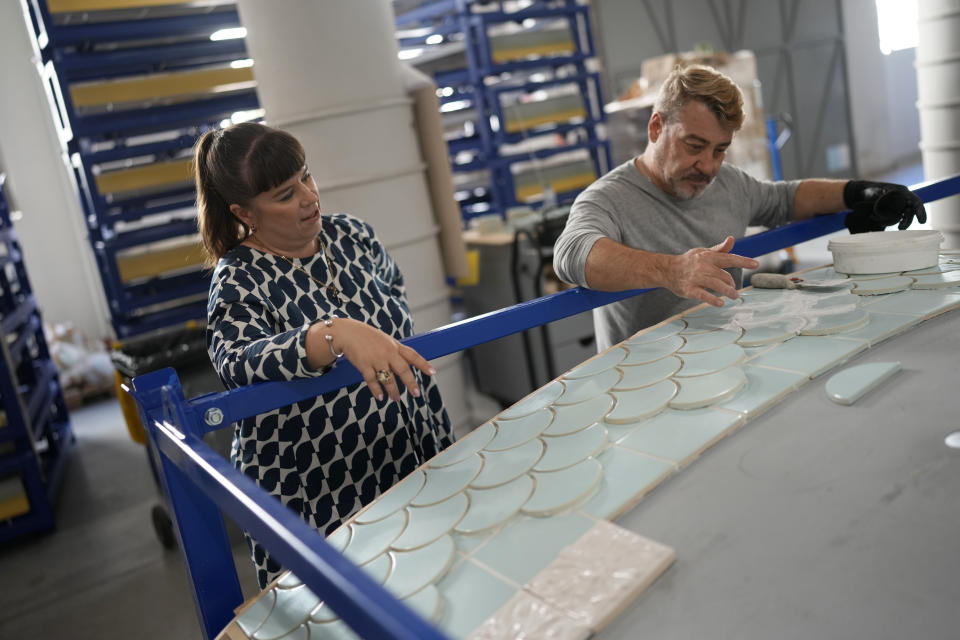 Portuguese artist Joana Vasconcelos watches a worker glue ceramic tiles on a section of her 12 meters high and 15 meters wide ceramic wedding cake, at her studio in Lisbon, Friday, Nov. 11, 2022. The Wedding Cake, her most ambitious outdoor project yet, will be erected in the gardens of Waddesdon Manor in southeast England, which hosts weddings. (AP Photo/Armando Franca)