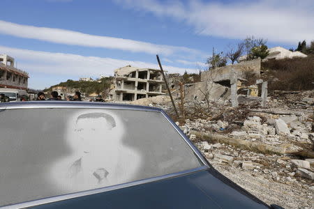 An image of Syria's President Bashar al-Assad is seen on a car parked in front of damaged buildings in the town of Rabiya, after pro-government forces recaptured the rebel-held town in coastal Latakia province, Syria January 27, 2016. REUTERS/Omar Sanadiki