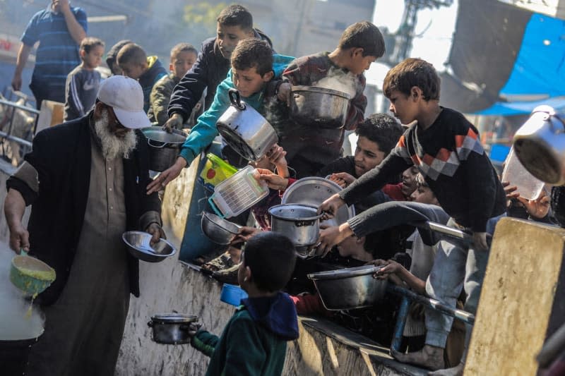 Palestinians gather with pots to receive food at a donation point provided by a charitable organization in Rafah in the southern Gaza Strip. Mohammed Talatene/dpa