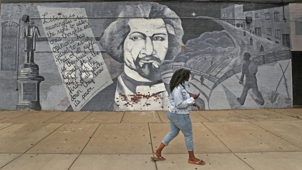 A woman, wearing a protective mask due to the COVID-19 virus outbreak, walks past a mural in tribute to Frederick Douglass on Wednesday, June 24, 2020, in the South End neighborhood of Boston. (AP Photo/Charles Krupa)