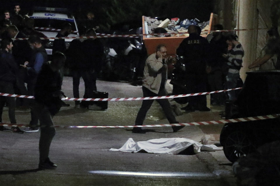 In this photo taken on Wednesday, Oct. 31, 2018, photo police officers stand over the covered body of Greek-Australian John Macris who was shot dead outside his house in southern Athens. Police are investigating the shooting death of a 46-year-old Greek-Australian who was gunned down outside his home in a seaside suburb of Athens. An autopsy on the body of John Macris was to be carried out Thursday. (Giorgos Kontarinis/Eurokinissi via AP)