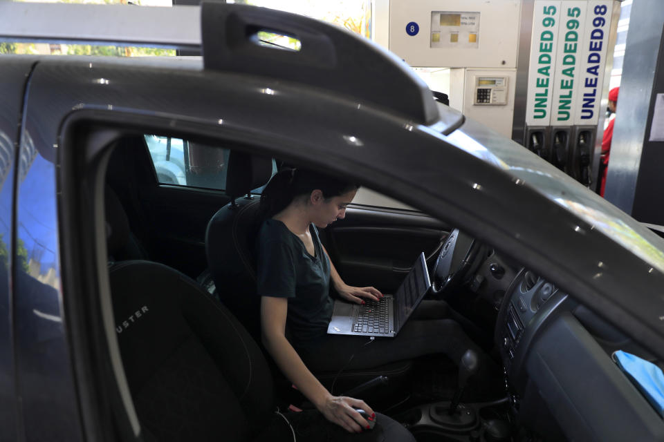 An employee save time by works on her laptop while she waits on a long queue to fill her car with gasoline in Beirut, Lebanon, Friday, June 25, 2021. Lebanon's caretaker prime minister on Friday granted his approval to allow the financing of fuel imports at a rate higher than the official exchange rate, effectively reducing critical fuel subsidies that have been in place for decades, amid worsening gasoline shortages. (AP Photo/Hussein Malla)