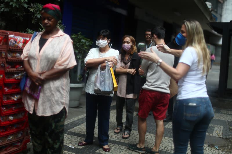 Una trabajadora bancaria pide a clientes mantener la distancia mientras esperan ingresar a la sucursal en medio del brote de coronavirus, en Río de Janeiro, Brasil