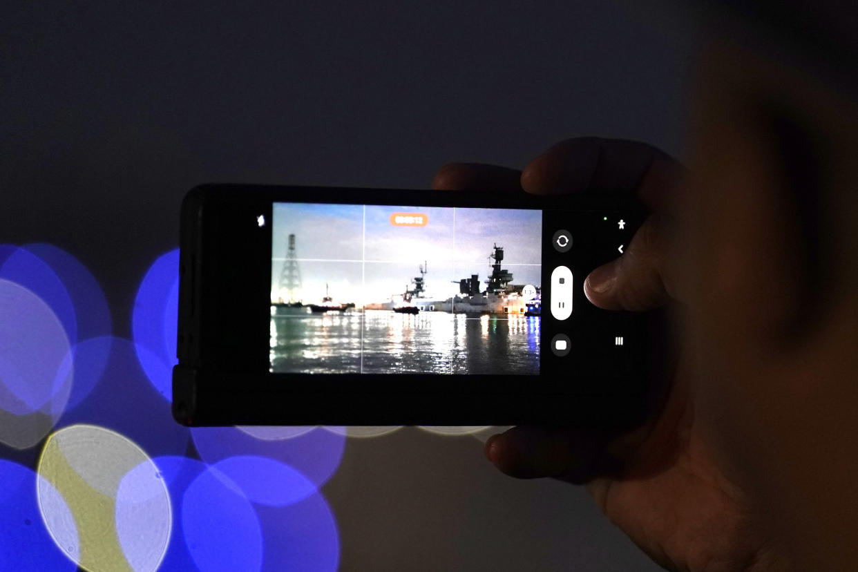 Texas Department of Public Safety Trooper Jose Chapa films the USS Texas with his phone as it is moved away from the dock Wednesday, Aug. 31, 2022, in La Porte, Texas. The vessel, which was commissioned in 1914 and served in both World War I and World War II, is being towed down the Houston Ship Channel to a dry dock in Galveston where it will undergo an extensive $35 million repair. (AP Photo/David J. Phillip)