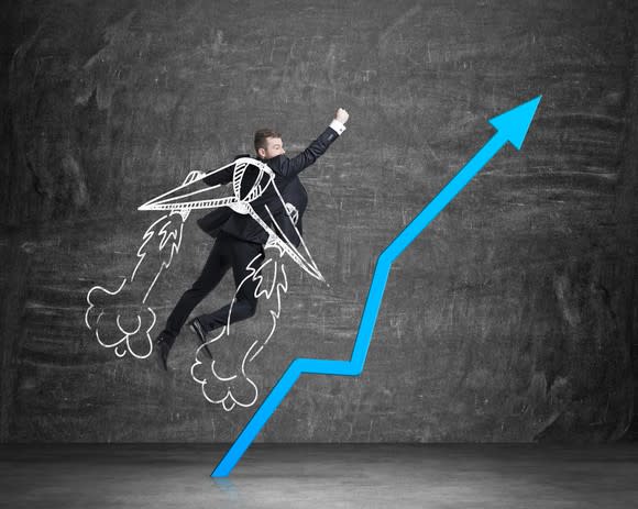 Businessman with chalk drawings of wings on his back jumping next to line chart pointing up.