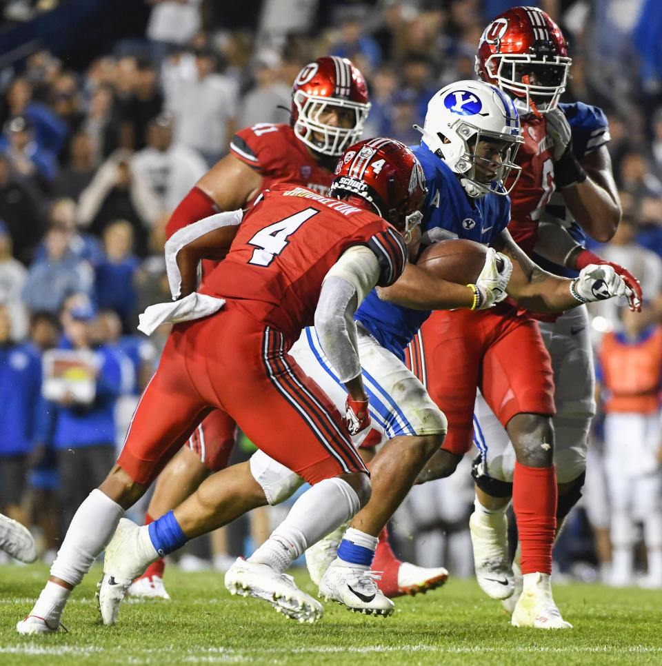 Brigham Young running back Tyler Allgeier, center, runs between Utah cornerback JaTravis Broughton, left, and Utah linebacker Devin Lloyd, right, during the second half of an NCAA college football game Saturday, Sept. 11, 2021, in Provo, Utah. (AP Photo/Alex Goodlett)