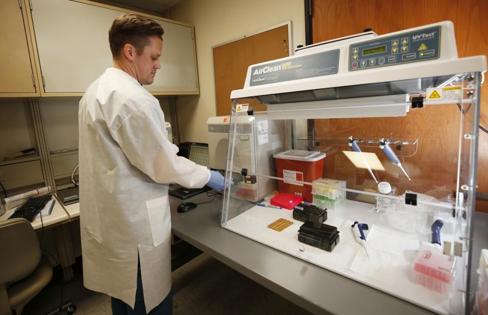 A man in a white lab coat stands next to a machine