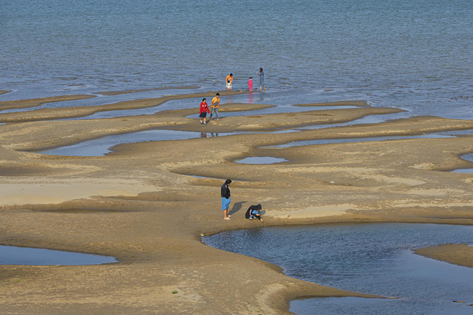 In this Wednesday, Dec. 4, 2019, photo, sightseers plays on a sandbar in the Mekong River in Nakhon Phanom province, northeastern Thailand. Experts say the aquamarine color the Mekong River has recently acquired may beguile tourists but it also indicates a problem caused by upstream dams. The water usually is a yellowish-brown shade due to the sediment it normally carries downstream. But lately it has been running clear, taking on a blue-green hue that is a reflection of the sky. The water levels have also become unusually low, exposing sandbanks in the middle of the river. (AP Photo/Chessadaporn Buasai)