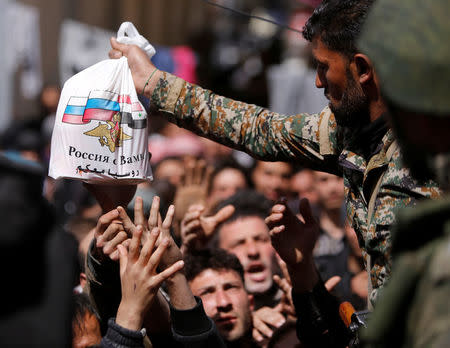 A Syrian army soldier distributes aid from Russian forces to civilians who fled eastern Ghouta, at a shelter in Adra near Damascus, Syria, March 20, 2018. REUTERS/Omar Sanadiki