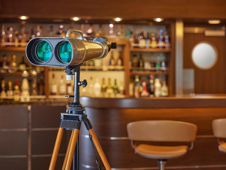 A set of golden binoculars with green lens in front of a bar scene.