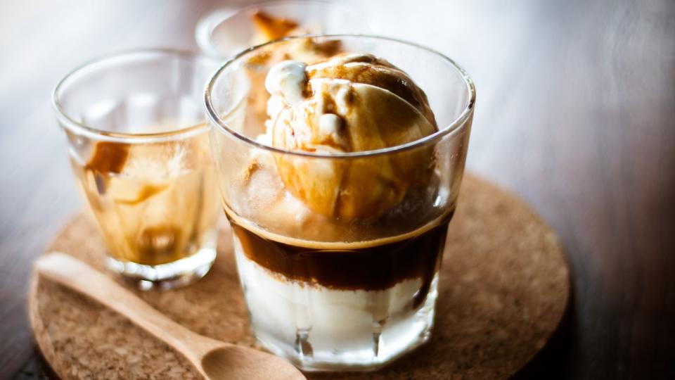 An affogato in a glass on a cork board with a wooden spoon