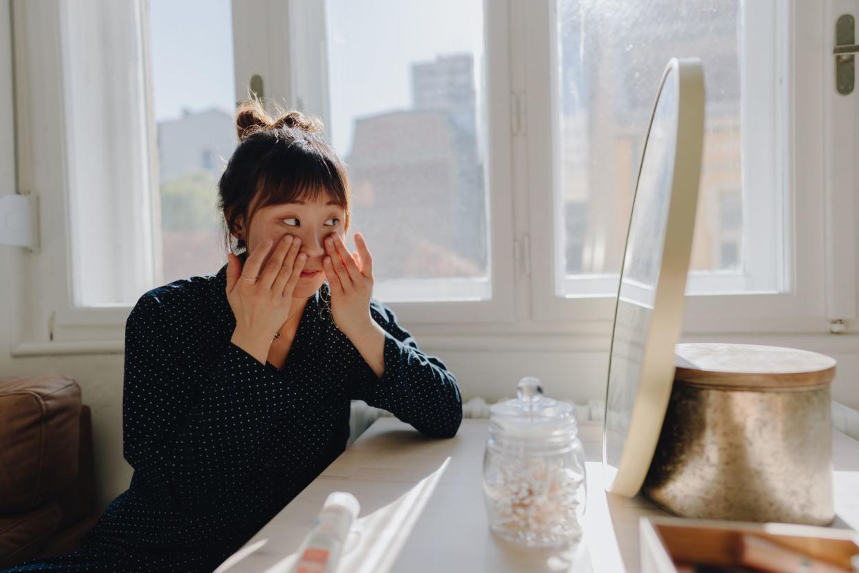 Photo of a young woman doing her skincare routine at home; applying moisturizer and getting ready for the upcoming day.